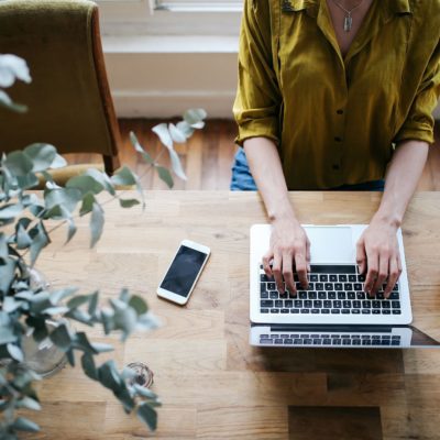 image of person at table with laptop, phone, and coffee, typing