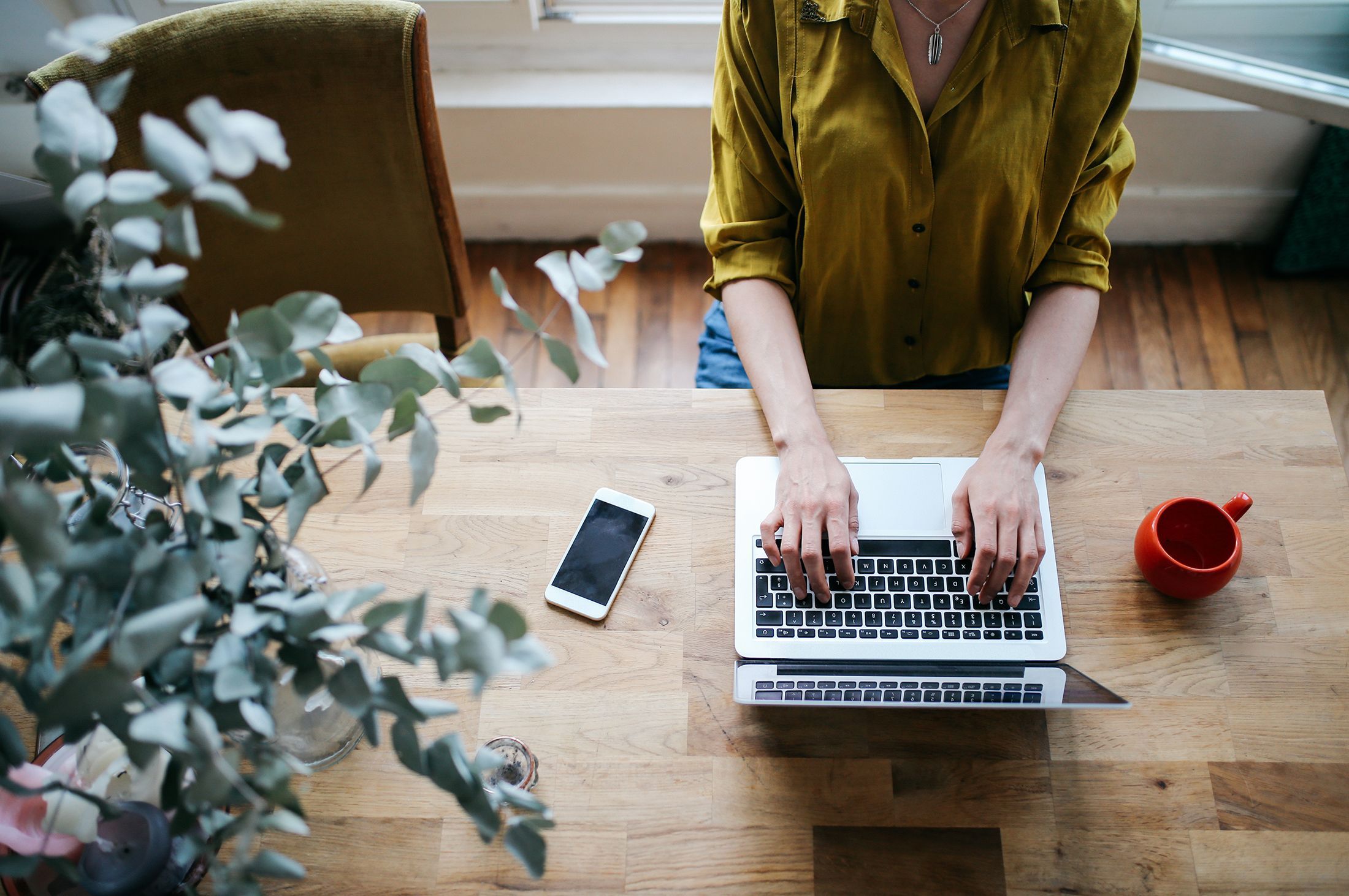 image of person at table with laptop, phone, and coffee, typing
