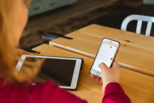 Image of woman holding phone with calendar open and ipad nearby