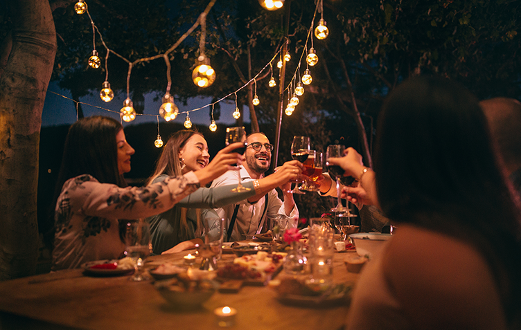 group of people toasting at dinner in an outdoor table with string of lights